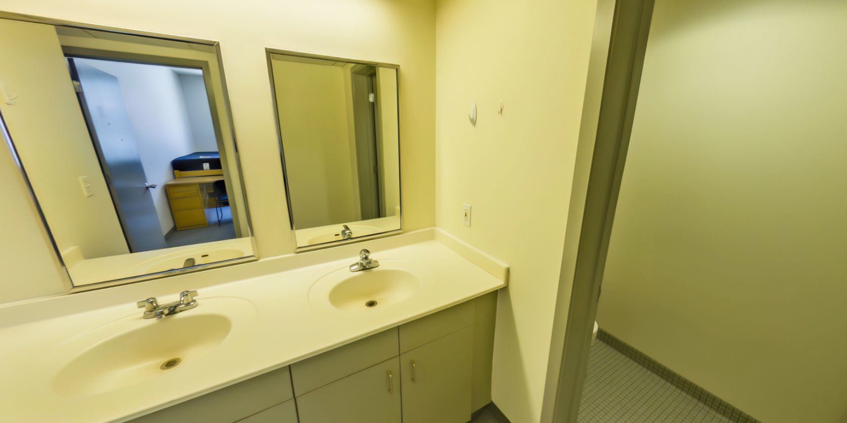 This side of the second hallway connects to a bathroom with a tiled floor, double vanities, and a toilet.