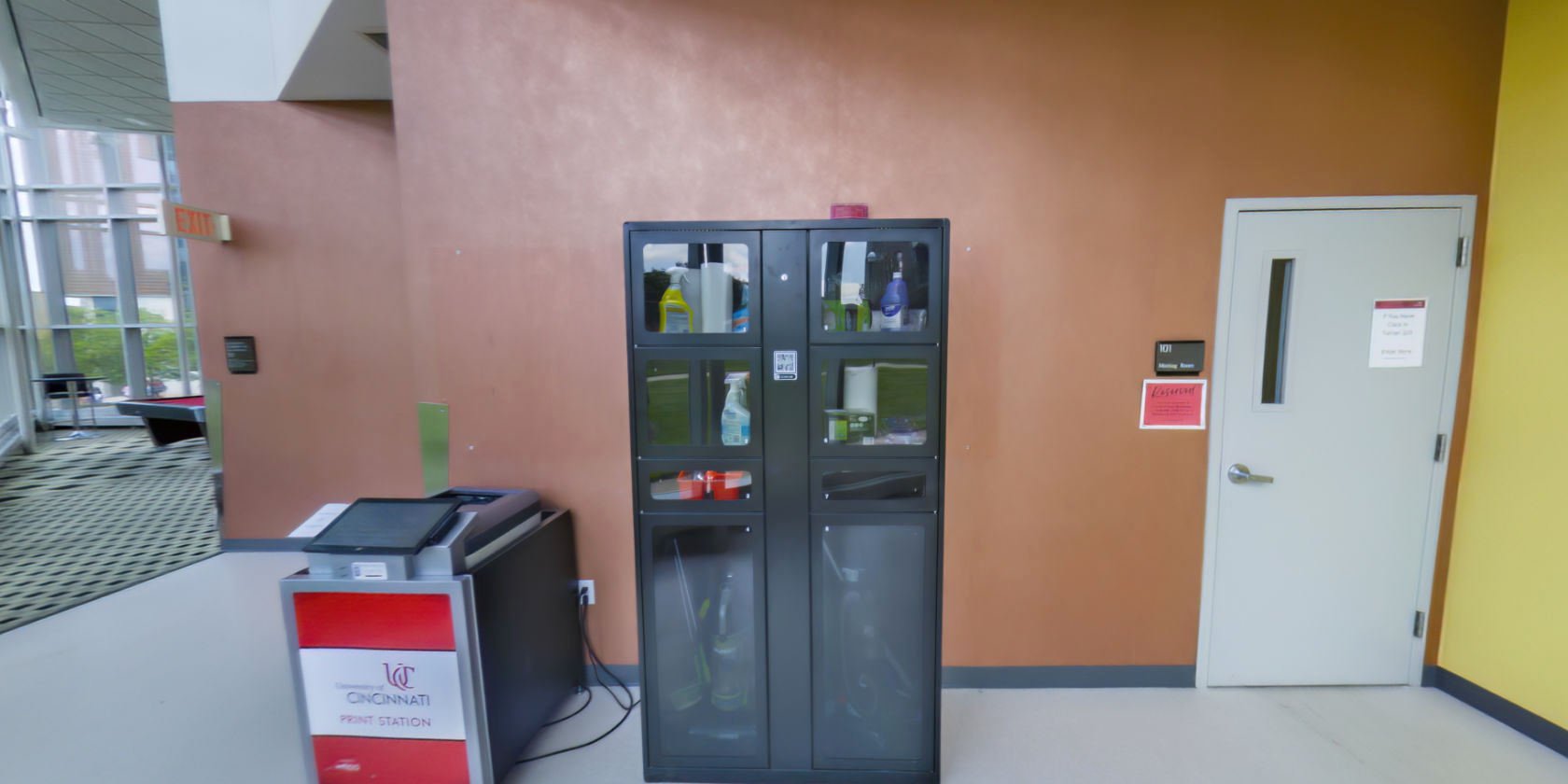 This side of the breakout room has a tiled floor, access to a meeting room, a University of Cincinnati Print Station, and a RecRe box stocked with cleaning supplies.