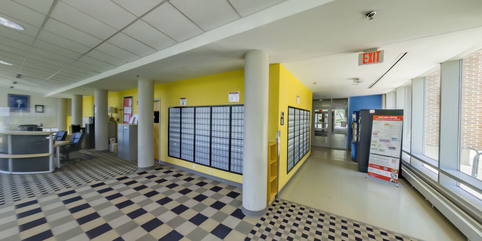 This side of the lobby leads to a tiled hallway with several Pepsi vending machines and windows with a campus view.