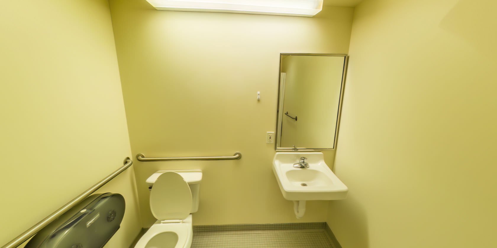 This bathroom has a tiled floor, a single vanity, and a toilet with grab bars.