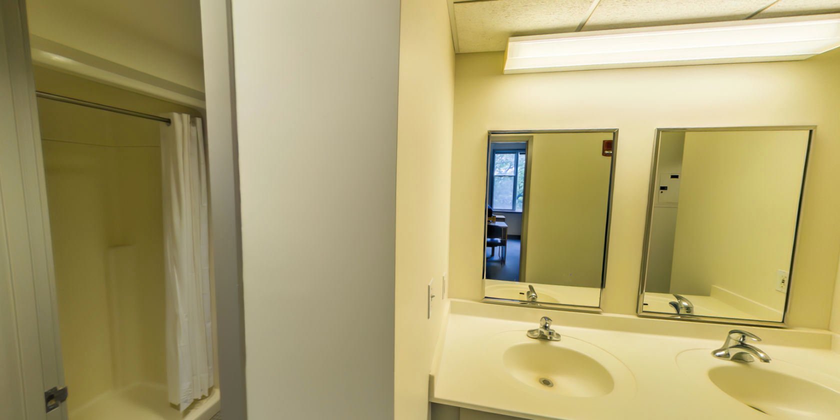 This side of the hallway connects to a tiled bathroom with a walk-in shower and access to an area with double vanities.
