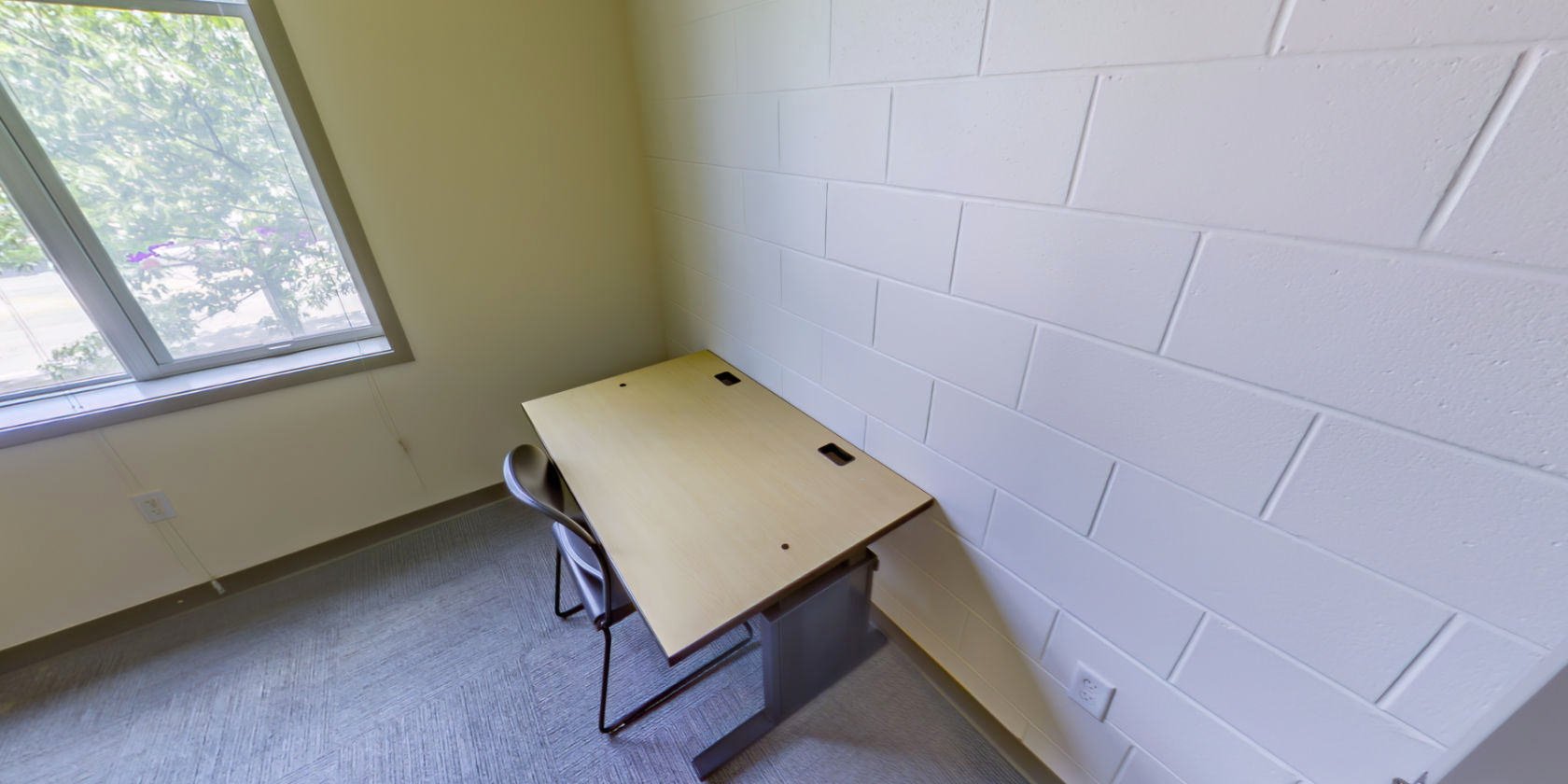 This side of the bedroom has a desk and shaded windows with a view overlooking the campus.