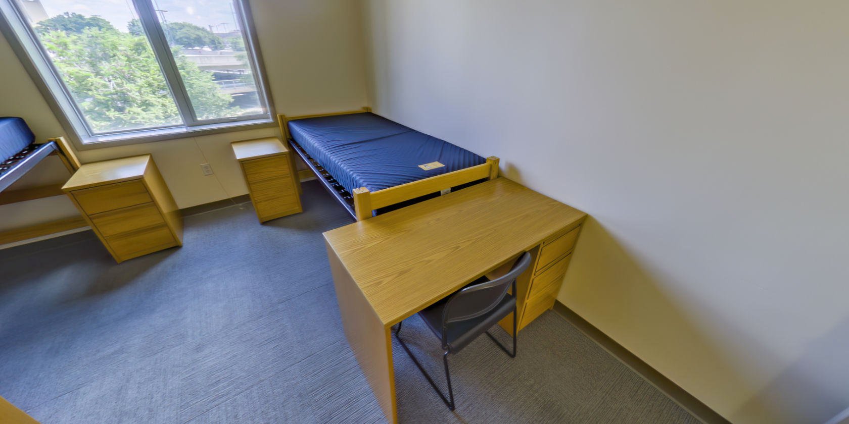 This side of the bedroom has a second single bed with space below for storage and a second desk with drawers. There is a second piece of bedside storage next to the bed.