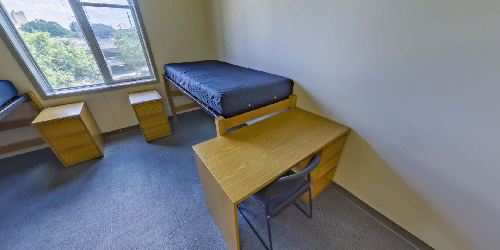 This side of the bedroom has a second single bed with space below for storage and a second desk with drawers. There is a second piece of bedside storage next to the bed.